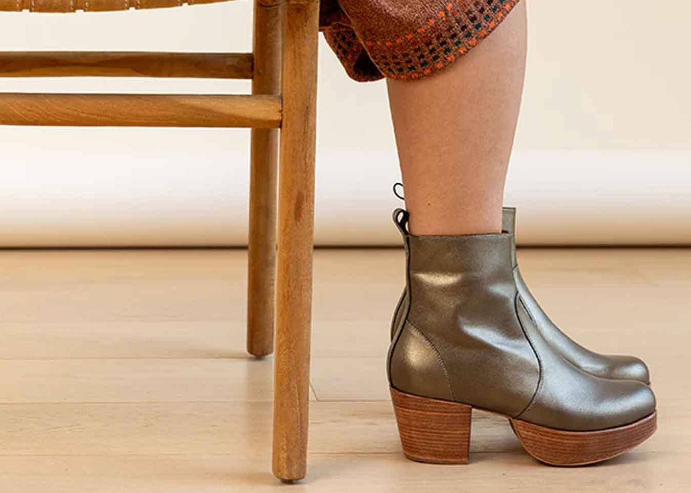 Person wearing green boots standing next to a wooden chair on a wooden floor.